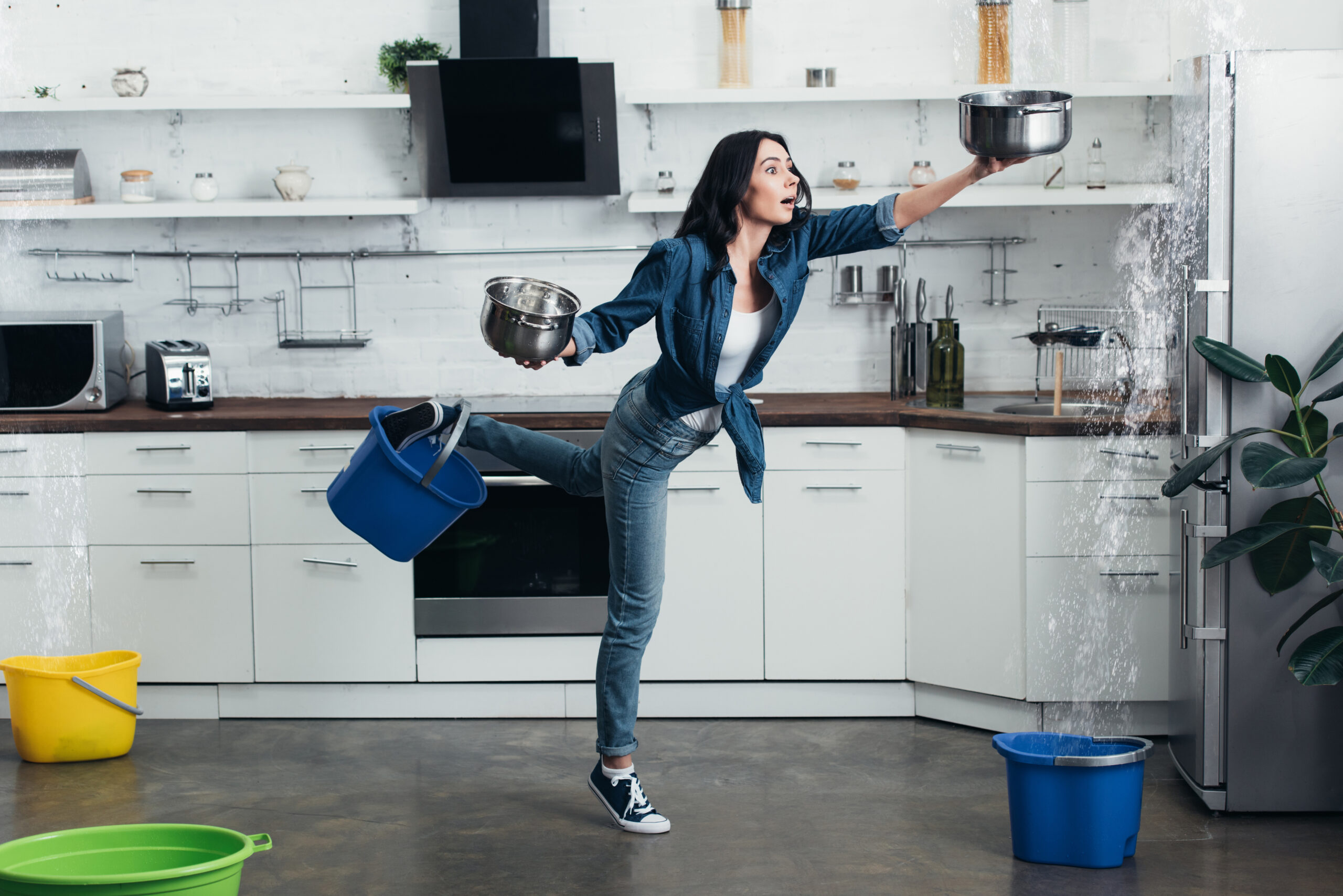 Full length view of shocked woman in jeans dealing with water leak in kitchen